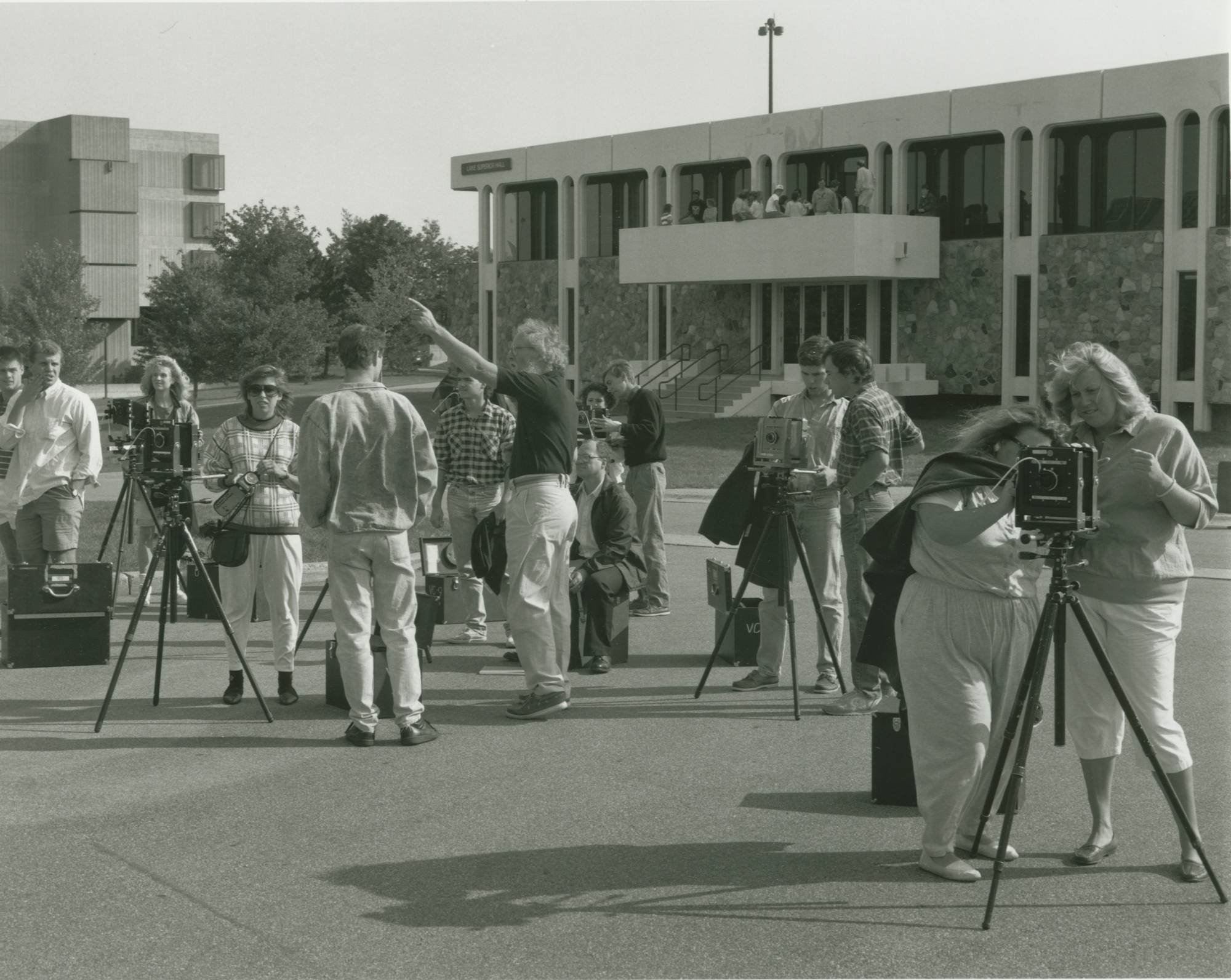 Students and faculty taking photos with cameras on tripods in front of Lake Superior Hall on a sunny day.